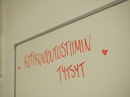 Det står "kotikuntoutustiimin tytsyt" på en vit tavla. Efter texten finns ett litet hjärta.